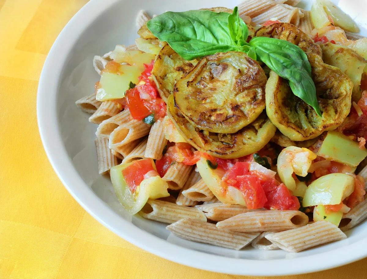 Penne with browned eggplant, tomato sauce and fresh basil on a white plate
